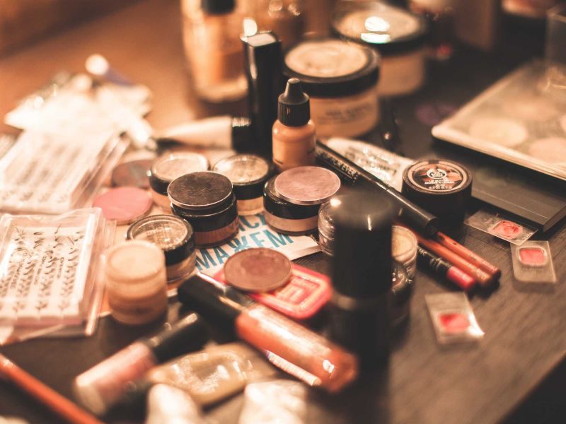 auf dem Bild sieht man bei gedimmten licht chaotisch verschiedene Makeup Produkte wie Puder, Lidschatten, Fake Lashes und Foundation verteilt