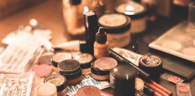 auf dem Bild sieht man bei gedimmten licht chaotisch verschiedene Makeup Produkte wie Puder, Lidschatten, Fake Lashes und Foundation verteilt